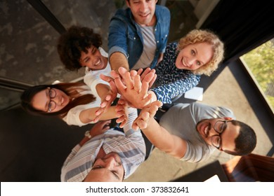 Top View Of Successful Team Of Professionals High Fiving And Looking At Camera Smiling. Men And Women Making A Pile Of Hands In Office.