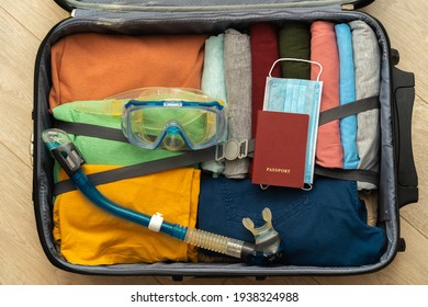 Top view of a suitcase prepared for a seaside holiday during a pandemic. Clothes neatly folded, passport with medical and snorkelling mask and snorkel. The concept of a safe seaside holiday