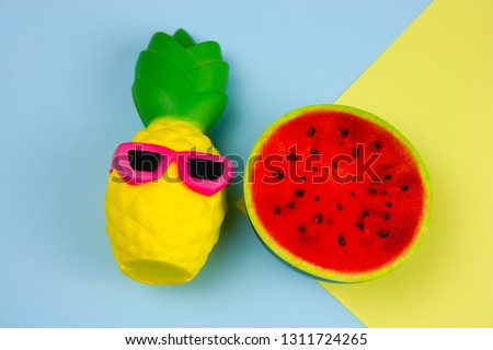top view summer vibrant blue and yellow  background with funny pineapple toy in sunglasses and squishy toy watermelon