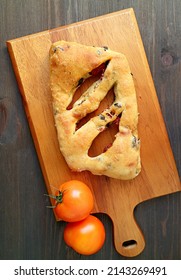 Top View of Sun Dried Tomato and Olive Fougasse French Bread on Wooden Breadboard with Two Fresh Tomatoes