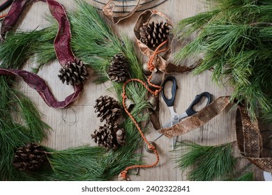 Top view of supplies and layout for making a Christmas wreath with fresh pine branches, ribbon and pine cones. - Powered by Shutterstock