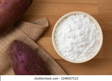 Top view of sweet potato starch in white bowl with sweet potato wooden table background