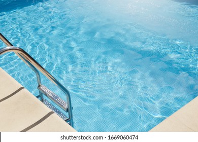 Top View Of Swimming Pool With Clear Blue Water, Metal Stairs Into Pool, No People Inside, Transparent Water, Sunlight, Having Sunny Day, Summer And Rest Conept, Spa Resort Conditions. Rest Concept.