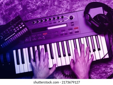 Top view of synthesizer keyboard piano with male hands in neon light. Music maker equipment.