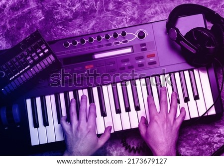 Top view of synthesizer keyboard piano with male hands in neon light. Music maker equipment.