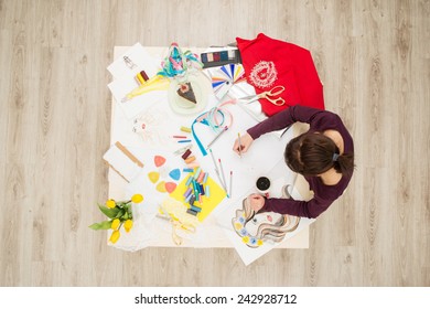 Top view of table full of creative things with young woman drawing. Fashion designer concept