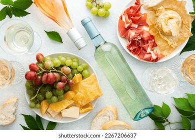 Top view of table with rose and white wine in glasses, plates with grapes, cheese and jamon, baked camembert cheese and baguette, tasting party or cozy dinner with wine - Powered by Shutterstock