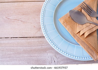 Top view of the table setting with a plate, cutlery and brown napkin on wooden table.