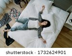 top view of taiwanese woman lying in a sprawl on bed with her clothes scattered on floor. asian young girl hanging out with friend until dawn goes to bed straight without taking bath.