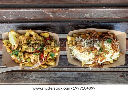 Top view of take away portions of  fancy poutine, French fries on top with spicy chicken, cheese and pulled pork, on outdoor wooden bench.