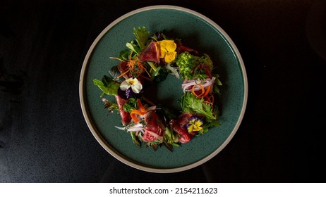 Top view of Tartare beef flower circle salad in the fine dining Japanese restaurant, with a green round plate in black scene reflection table background, raw beef, onion, salad, carrot, flowers - Shutterstock ID 2154211623