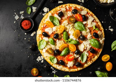 Top View Of Tasty Appetizing Classic Italian Traditional Pizza With Cheese, Olives, Basil And Fresh Vegetables On Dark Black Table. 