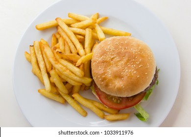 Top View Of Tasty Beef Burger With French Fries On The Side. Hamburger With Tomato, Lettuce And Potatoes On White Plate From Above. Poor Nutritional Meal Concept