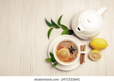 top view tea and cinnamon a cup of herbal tea cinnamon sticks on the saucer lemon teapot and leaves on the white table - Powered by Shutterstock