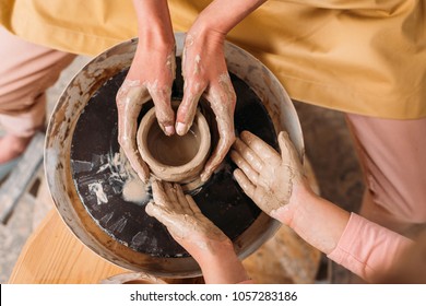 top view of teacher and kid making ceramic pot on pottery wheel