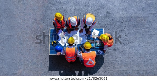 Top view of team of architectural engineer working,\
meeting, planning with blueprint, Solar photovoltaic equipment,\
wind turbine business important infrastructure on solar panel at\
construction site. 