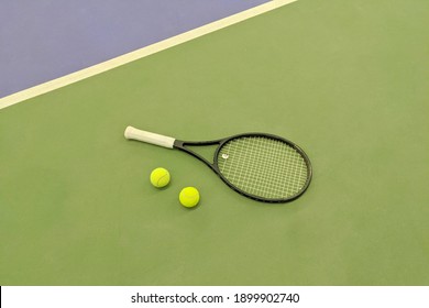 Top View Of Tennis Racket And Two Balls On The Green Clay Tennis Court.