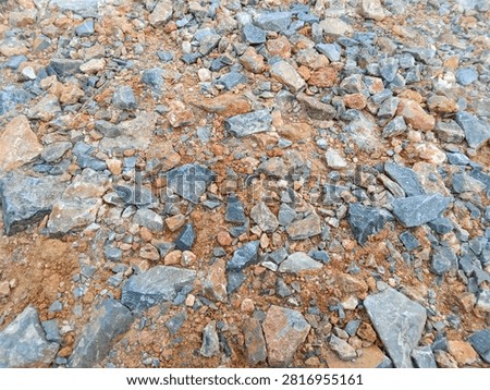 Top view texture of aggregate stones, pebbles, and orange dirt on the ground.