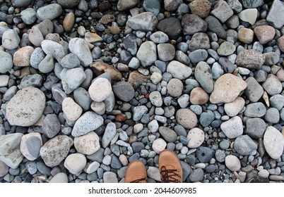 Top view of textures of rounded gray rocks on the shore of a lake, partially wet next to sneakers.