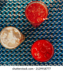 Top view of three different delicious summer cocktails with icecubes on table, glasses with cold refreshing fruit drinks on blue tablecloth