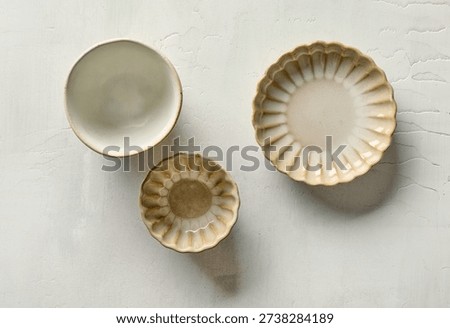 Top view of three empty decorative small ceramic bowls placed on a light painted kitchen table surface. Minimal and cozy composition suitable for kitchen, home decor, tableware, and lifestyle concepts