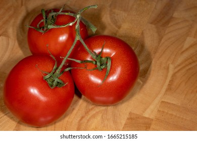 Top view of three red tomatoes on a brown wooden board