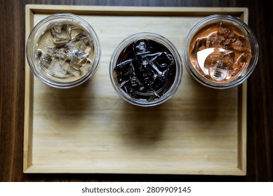 Top view of three refreshing iced latte, iced Americano and an iced Thai milk tea served on wood tray