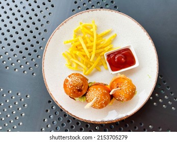 Top view of three tiny mini burgers, fried potatoes, and ketchup on a plate on the table. Fast. Tiny. Mini. Cafe. Cooked. Circle. Restaurant. Original. Nourishment. Serving. Freshness. Plate. Rustic