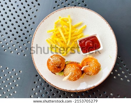 Top view of three tiny mini burgers, fried potatoes, and ketchup on a plate on the table. Fast. Tiny. Mini. Cafe. Cooked. Circle. Restaurant. Original. Nourishment. Serving. Freshness. Plate. Rustic
