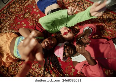 Top view of three trendy young people lying on ornate carpet in circle and looking at camera - Powered by Shutterstock