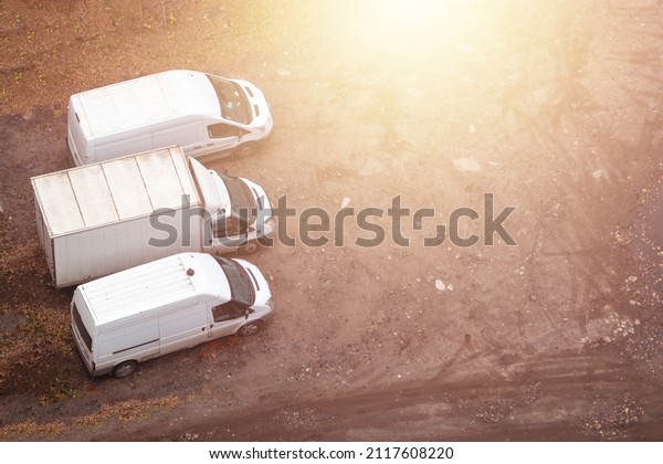Top view of three white truck vans\
parked on warehouse area. Copy space. Yellow\
glow.