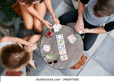 Top view of three young people playing cards at sidewalk cafe. Young people sitting around a coffee table and playing card game.