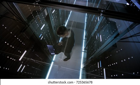 Top View Through the Glass of IT Engineer Working with Laptop in Data Center Full of  Active Rack Servers.