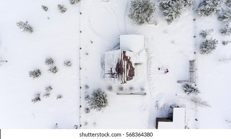 Top View At The Timber House Under Snow In Countryside. Courtyard With People Playing In Snowdrift. 