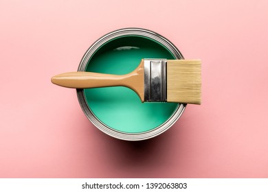 top view of tin of green paint and brush on pink surface