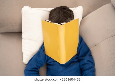 Top view tired and book with a student lying on the sofa in his living room, sleeping in a house. Learning, exhausted and reading with a college student asleep in a house while studying - Powered by Shutterstock