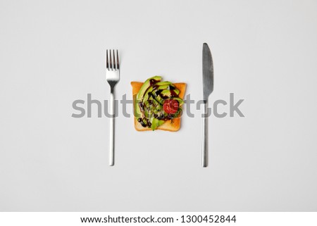 top view of toast with avocado and cherry tomato, fork and knive isolated on grey