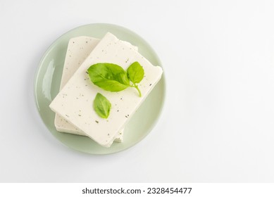 Top view of  tofu, paneer or soy cheese with fresh basil leaves in a green plate isolated with copy space