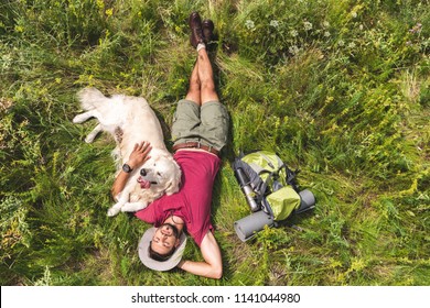 top view of tourist and golden retriever dog lying on green grass with backpack