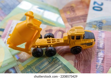 Top View Of A Toy Concrete Mixer On The Background Of Different Euro Banknotes. The Concept Of Expensive Modern Construction.