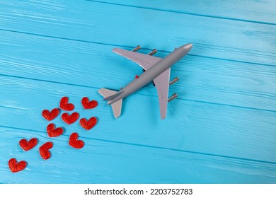 Top View Of Toy Passenger Boeing Plane With Red Hearts. Blue Wooden Desk Surface.