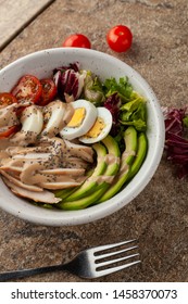 Top View Of Traditional American Cobb Salad With Avocado, Chicken Breast, Vinaigrette, Tomatoes And Hard Boiled Egg, Served On A Marble Table With Different Ingredients Around