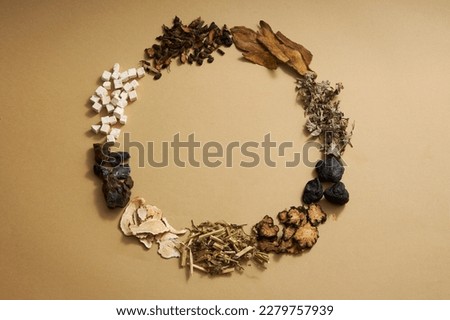 Top view of traditional Chinese medicines arranged in a circle on light brown background. Herbs to help supplement and enhance health. Empty space for text and design.