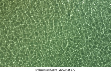 Top view of transparent water sea with stone and pebbles bottom. Sun glare on the surface crystal clear emerald water, swaying in the wind. Natural summer sea background texture.