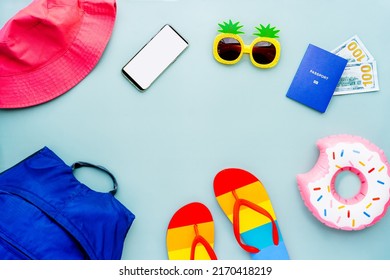 Top view travel summer vacation concept with backpack, bucket hat, funny sunglasses, flip flops, inflatable donut, biometric passport, money and phone with blank screen. Flat Lay with copy space.