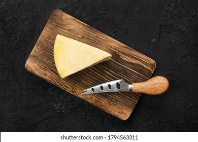 Top View Of Triangular Piece Of Hard Cheese On Wooden Cutting Board