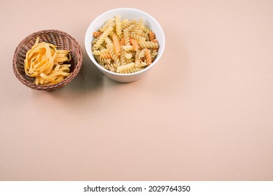 A Top View Of Tri-color Rotini And Fettuccine Pasta On A Bowl Isolated On Brown Background