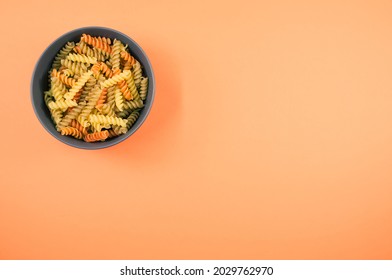 A Top View Of Tri-color Rotini Pasta On A Bowl Isolated On An Orange Background