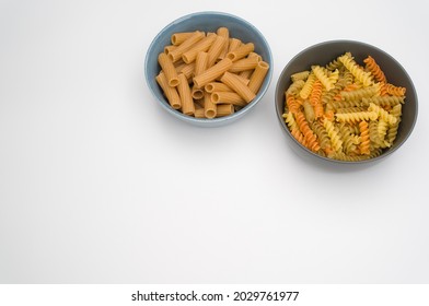 A Top View Of Tri-color Rotini And Rigatoni Pasta On Bowls Isolated On White Background