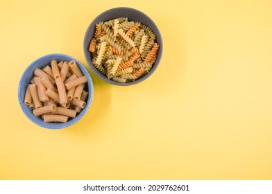 A Top View Of Tri-color Rotini And Rigatoni Pasta On A Bowl Isolated On Yellow Background